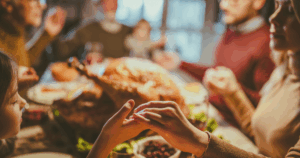 Close up of a mother and daughter holding hands while saying grace before the family’s Thanksgiving meal in the dining room.