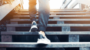 A person wearing sneakers and sweatpants ascends a wooden staircase.