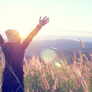 Happy Woman Enjoying Nature on grass meadow on top of mountain cliff with sunrise. Beauty Girl Outdoor. Freedom concept. Len flare effect. Sunbeams. Enjoyment.