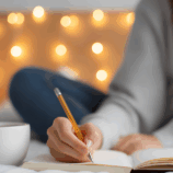 Woman sitting at a table journaling with a Bible beside her, symbolizing reflection, recovery, and faith in God.