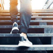A person wearing sneakers and sweatpants ascends a wooden staircase.