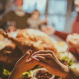 Close up of a mother and daughter holding hands while saying grace before the family’s Thanksgiving meal in the dining room.