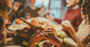 Close up of a mother and daughter holding hands while saying grace before the family’s Thanksgiving meal in the dining room.
